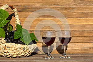 Two glasses of red wine and a basket of grapes on a wooden background on a Sunny day