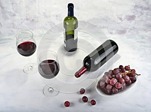 Two glasses of red wine with bottle and grapes.