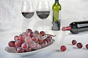 Two glasses of red wine with bottle and grapes.