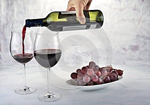 Two glasses of red wine with bottle and grapes.