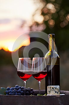 Two glasses of red wine and bottle at sunset