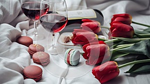 Two glasses of red wine, a bouquet of red tulips, chocolate and a bottle of wine on the bed. Free space for display.