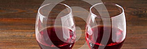Two glasses of red wine on a brown wooden table. Alcoholic beverages. banner