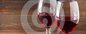 Two glasses of red wine on a brown wooden table. Alcoholic beverages.. Banner