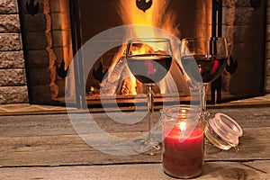 Two glasses of red wine and candle near cozy fireplace, in country house, winter vacation, horizontal