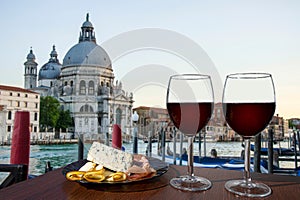 Two glasses of red wine with charcuterie assortment on gondolas and Santa Maria della Salute. Glass of red wine with different