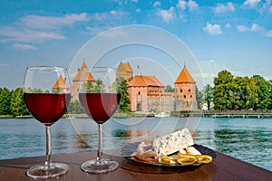 Two glasses of red wine with cheese and meat snacks with view of Trakai Island Castle near Vilnius, Lithuania. Beautiful