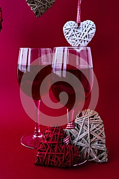 Two glasses of red wine and decorative hearts. Love romance. Couple relationship. Red matte background. White and red elements.