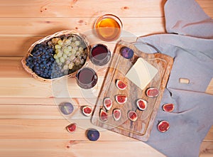 Two glasses of red wine, fig, cheese, bunches of grape and honey on wooden table