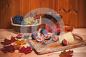 Glasses of red wine, fig, cheese, bunchs of grape, honey and colorful autumn maple leaves on wooden table. Selective focus