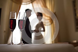 Two glasses of red wine in the foreground, and in the background the bride and groom