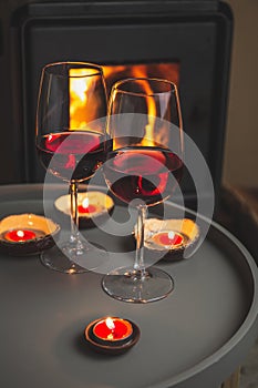 Two glasses of red wine front of fireplace. Romantic light