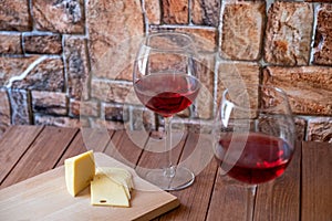 Two glasses of red wine and sliced cheese on a wooden table