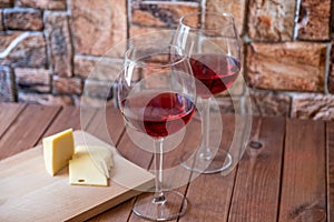 Two glasses of red wine and sliced cheese on a wooden table