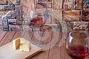 Two glasses of red wine and sliced cheese on a wooden table