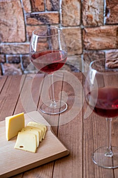 Two glasses of red wine and sliced cheese on a wooden table