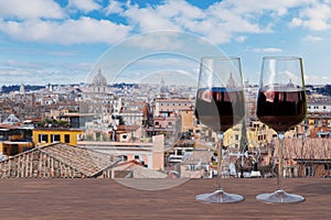 Two glasses of red wine on the table against view of Rome with a blue sky, showcasing the city\'s majestic skyline