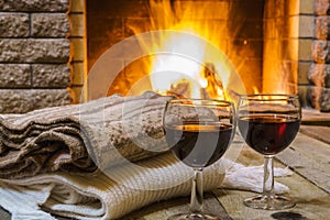 Two Glasses of red wine and woolen things near cozy fireplace.