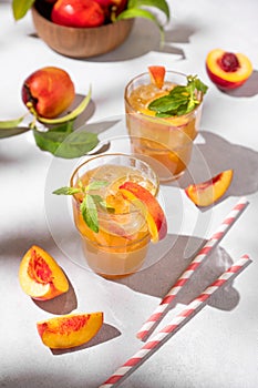Two glasses with refreshing peach tea with ice and mint. Homemade cold summer drink on a light background with fresh fruits and