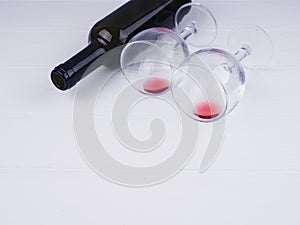 Two glasses with the remains and a bottle of wine lie on a white wooden background, a copy of the space