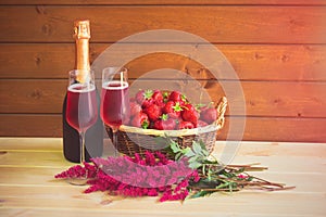 Two glasses of rose champagne, bottle of rose champagne, astilbe flowers and fresh strawberry in wicker basket