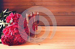 Two glasses of rose champagne and red peony flowers on wooden table. Selective focus