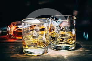 Dos anteojos de Escocia o conac cubitos a una botella de alcohol sobre el oscuro de madera 