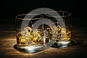 Two glasses of scotch whiskey or cognac and ice cubes on dark wooden background