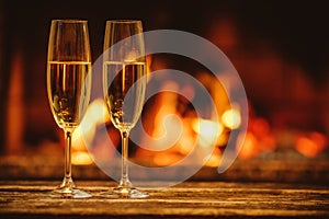 Two glasses of sparkling champagne in front of warm fireplace. C