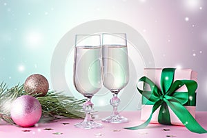 Two glasses of sparkling wine, gift box with bow, decorations. Composition in pink and green for Christmas, New Year. Still life