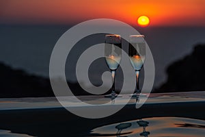 Two glasses of sparkling wine by the pool on a sunset background