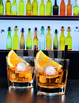 Two glasses of spritz aperitif aperol cocktail with orange slices and ice cubes on bar table, disco atmosphere background