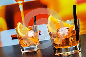 Two glasses of spritz aperitif aperol cocktail with orange slices and ice cubes on bar table, disco atmosphere background