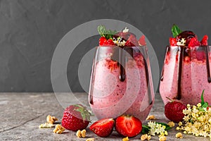 Two glasses of strawberry chia seed pudding with chocolate, fresh berries, granola, elderflowers and mint