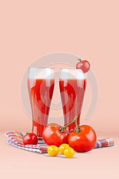 Two glasses with tomato juice and a small tomato on a bright background.