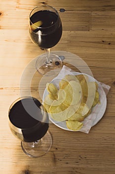 Two glasses of vermouth or cola drik and a plate of potatoes crisps on a wooden table a sunny day at a terrace