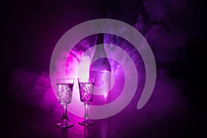 Two glasses of Vodka with bottle on dark foggy club style background with glowing lights (Laser, Stobe) Multi colored. Club drinks