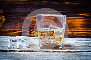 Two glasses of whiskey with ice cubes served on wooden planks. Vintage countertop with highlight and a glass of hard liquor delici