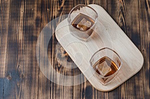 Two Glasses of whiskey with ice cubes on a wooden table/Two Glasses of cognac with ice cubes on a wooden table. Top view,