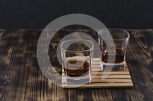 Two Glasses of whiskey with ice cubes on a wooden table/Two Glasses of whiskey with ice cubes on a wooden table. Black background