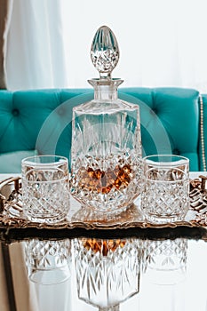 Two glasses of whiskey with ice and decanter on a wooden table