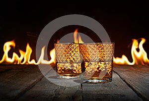 Two glasses of whiskey on a wooden table in front on a fire flame