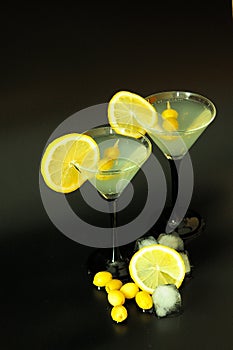 Two glasses of white vermouth with lemon wedges and olives on a black background with ice