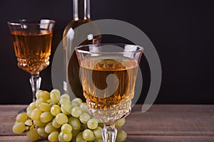 Two glasses of white wine, bottle and bunch of grapes standing on a wooden table