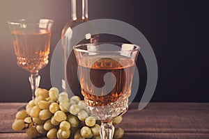 Two glasses of white wine, bottle and bunch of grapes standing on a wooden table