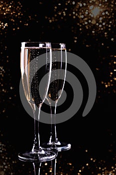 Two glasses with white wine champagne on a black background with golden bokeh.  Festive concept