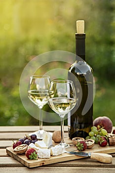 Two glasses of white wine, cheese, fruits. Romantic outdoor dinner in a garden