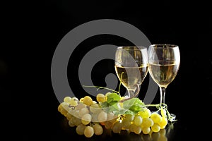 Two glasses of white wine and grape on black background