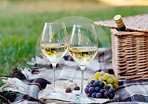 Two glasses of white wine and wooden plate with cheese and grapes served outside