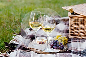 Two glasses of white wine and wooden plate with cheese and grapes served outside